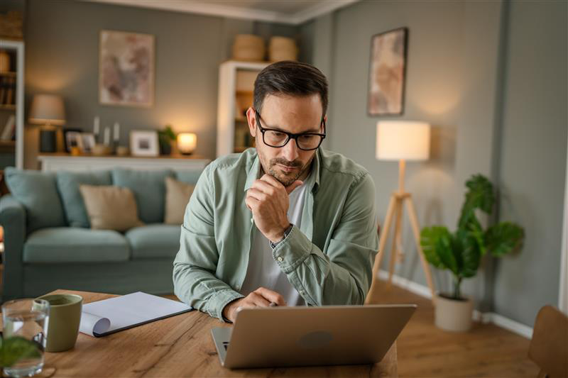 Uomo al computer durante una sessione di smart working da casa, in postura riflessiva