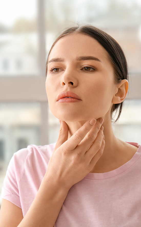 Donna si tocca la gola nella zona della tiroide, possibile sintomo di disfunzione endocrina o disturbo ormonale