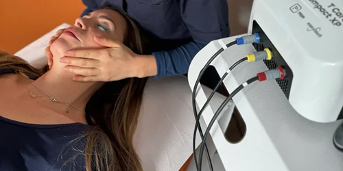Donna distesa riceve un trattamento estetico viso con manipolazione manuale e apparecchiatura per il miglioramento cutaneo