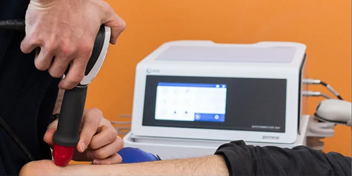Fisioterapista utilizza dispositivo a onde d’urto su un paziente per stimolare la rigenerazione dei tessuti muscolari e articolari