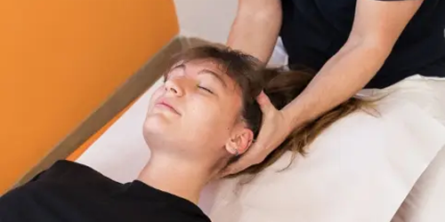 Osteopata esegue una terapia manuale sulla testa di una paziente sdraiata, per alleviare disturbi muscolo-scheletrici e migliorare la funzionalità del sistema nervoso