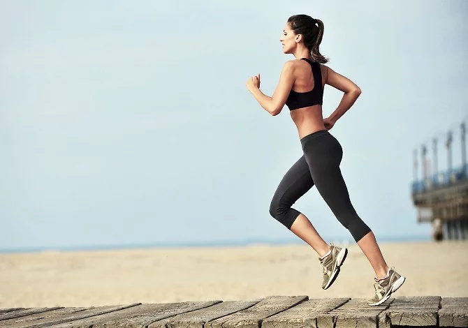 Giovane donna vestita sportiva che corre su una spiaggia