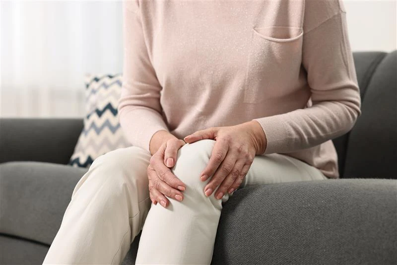 Donna che si tocca il ginocchio dolorante, mentre è seduta sul divano