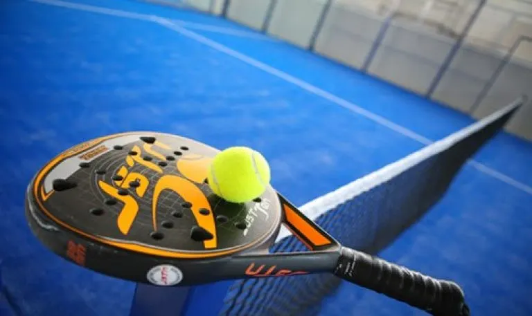 Racchetta di padel con pallina appoggiata sopra la rete