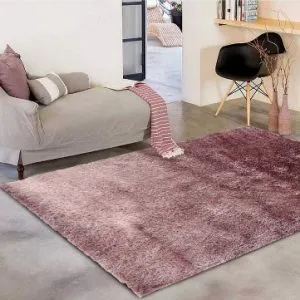 Salotto moderno con tappeto rosa sfumato, divano beige con cuscini coordinati, sedia nera e dettagli in legno chiaro su pavimento in cemento lucidato