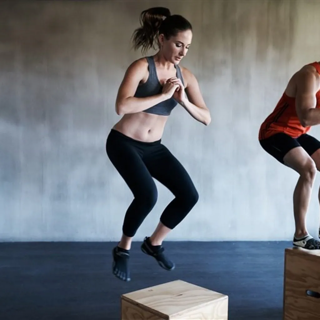 Donna in abbigliamento sportivo esegue esercizio di salto su box durante un allenamento funzionale
