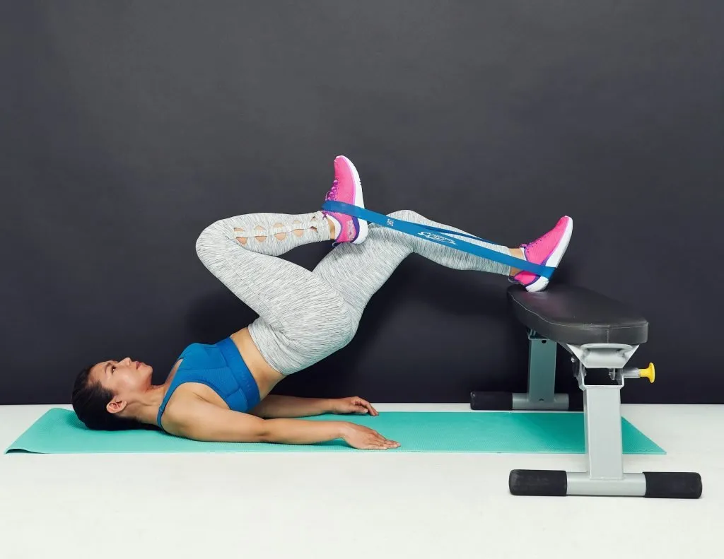 Donna sdraiata che esegue esercizi con elastico con gambe sollevate sullo step