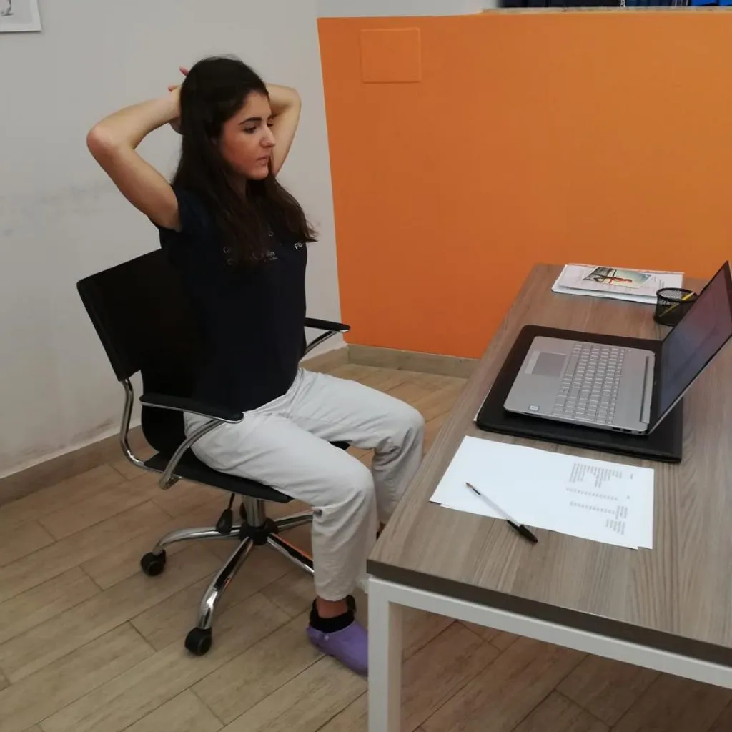 Donna seduta alla scrivania con le mani intrecciate dietro la testa, esegue esercizio di apertura toracica per migliorare la postura