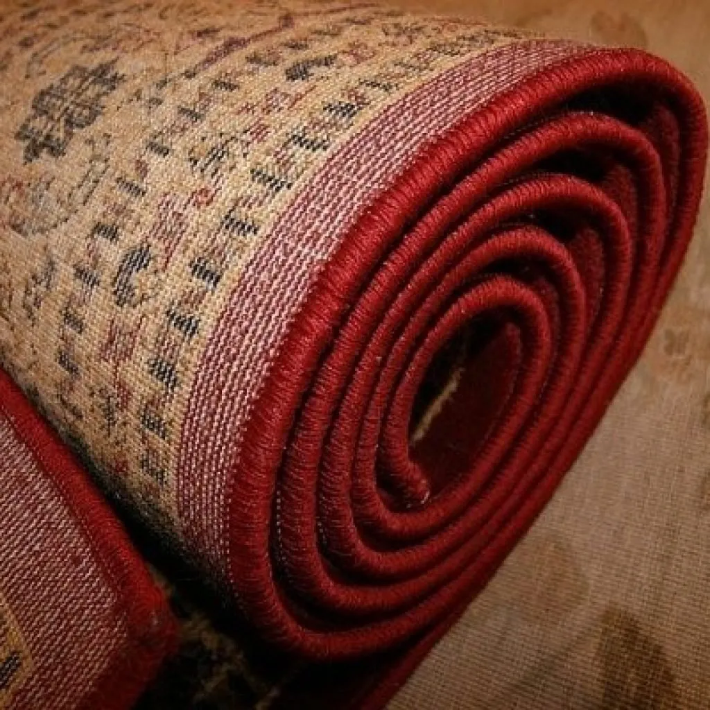 Tappeto orientale arrotolato con bordo rosso, dettaglio di tessitura e motivi decorativi