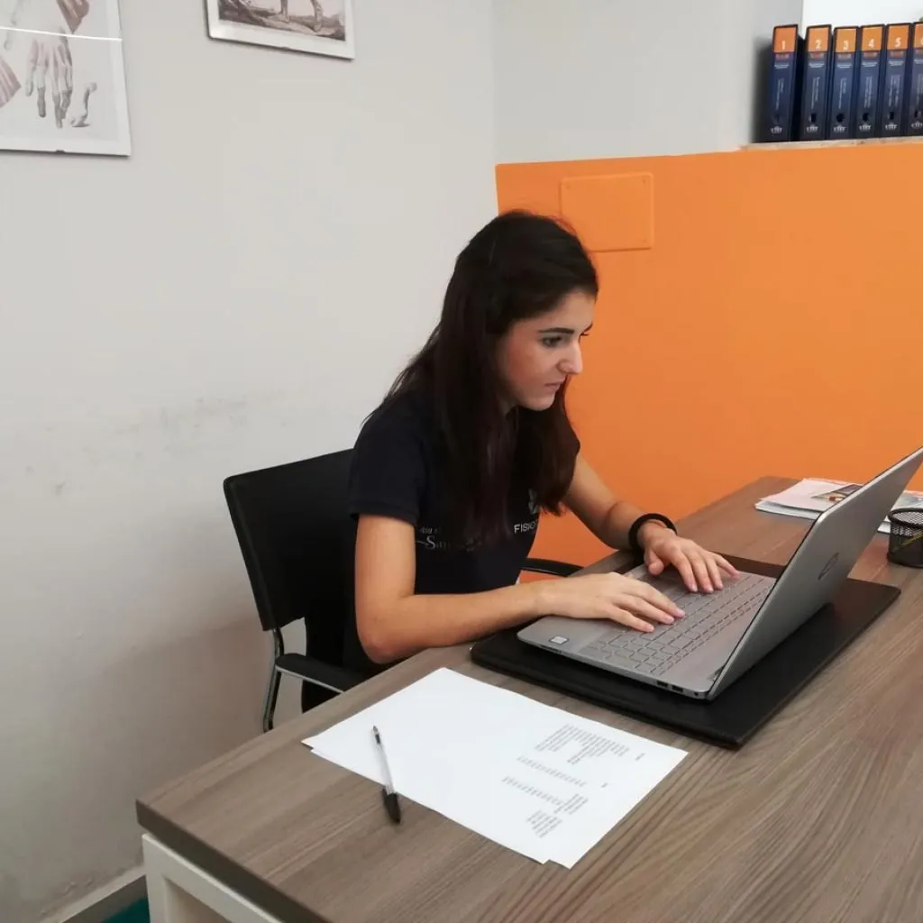 Giovane donna al computer seduta con postura scorretta alla scrivania, potenziale causa di mal di schiena da lavoro sedentario