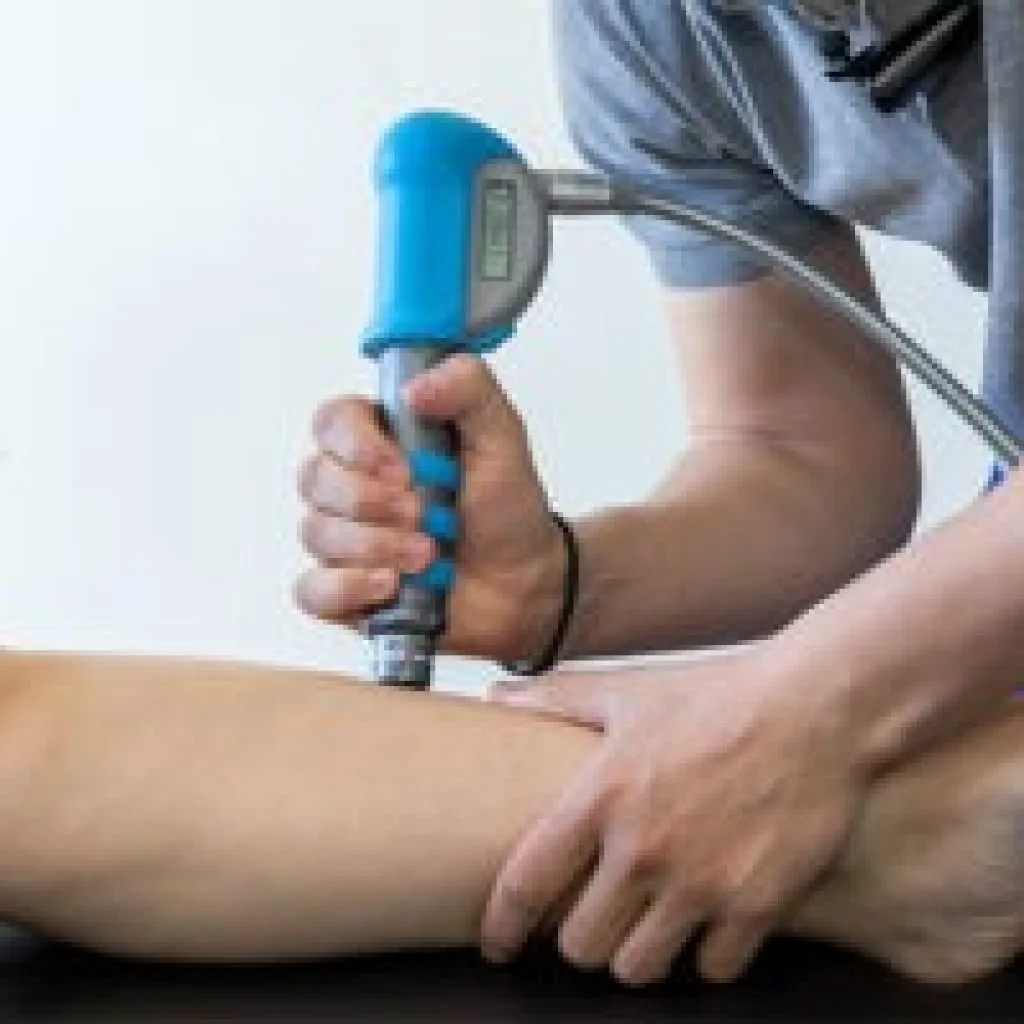 Fisioterapista esegue trattamento con onde d’urto su gamba di un paziente per curare infiammazioni muscolo-tendinee e dolori localizzati