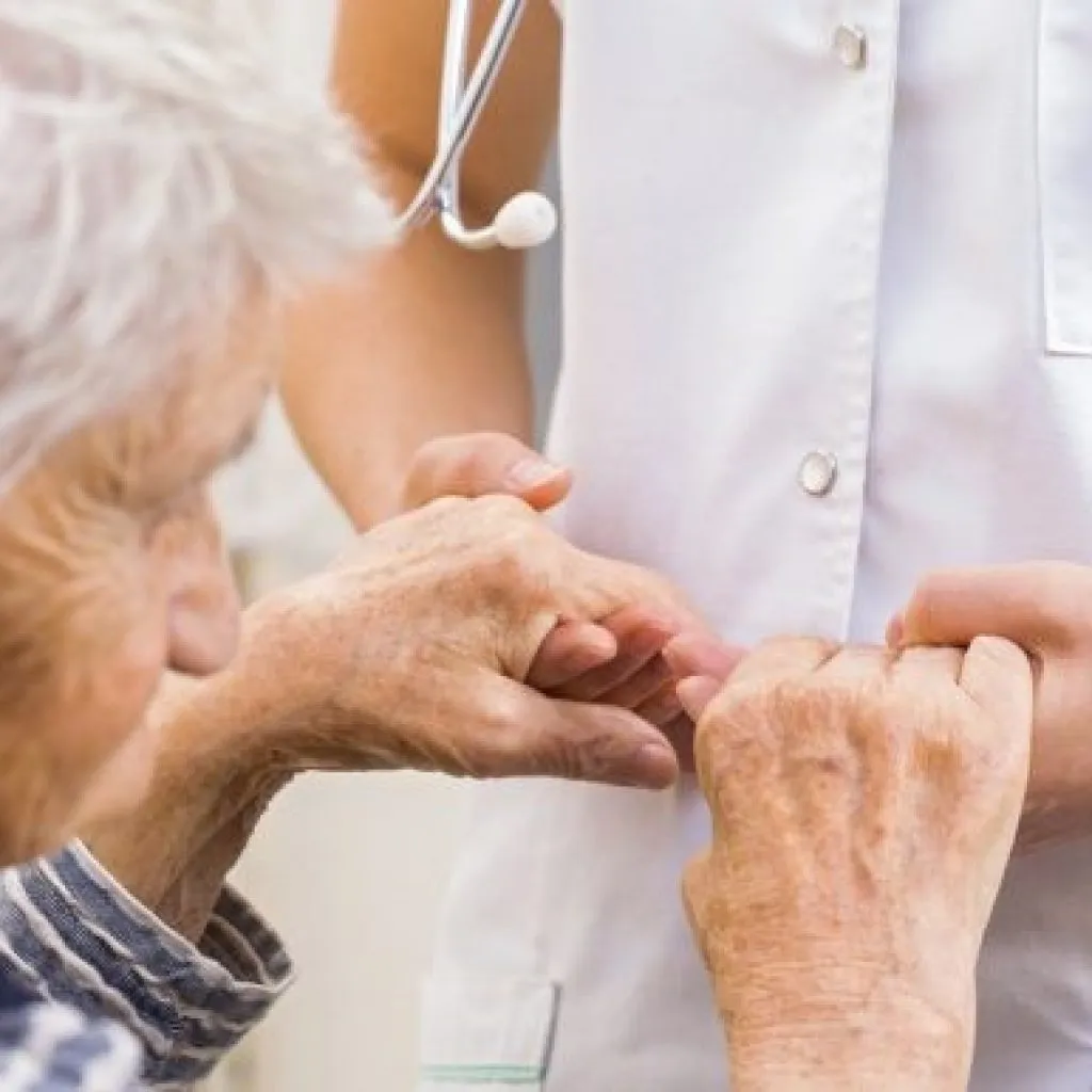 Operatore sanitario tiene le mani di un’anziana paziente in gesto di supporto e cura, simbolo di assistenza nei disturbi neurodegenerativi come il Parkinson