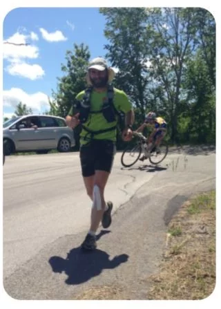 Corridore con zaino tecnico e taping al polpaccio durante gara su strada, seguito da ciclisti