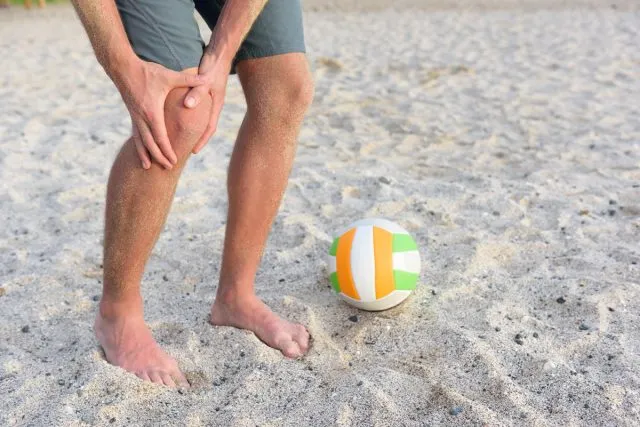 mani su ginocchio dolorante in spiaggia