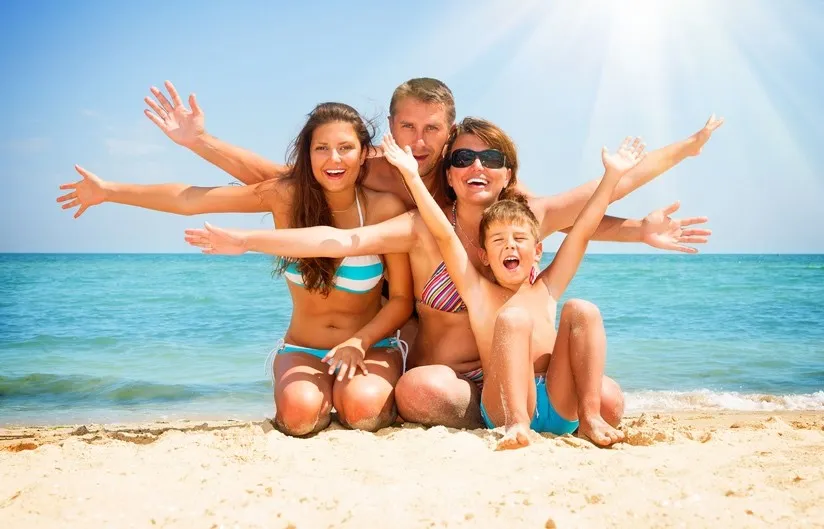 Famiglia sorridente in costume posa sulla sabbia con il mare sullo sfondo in una giornata d’estate